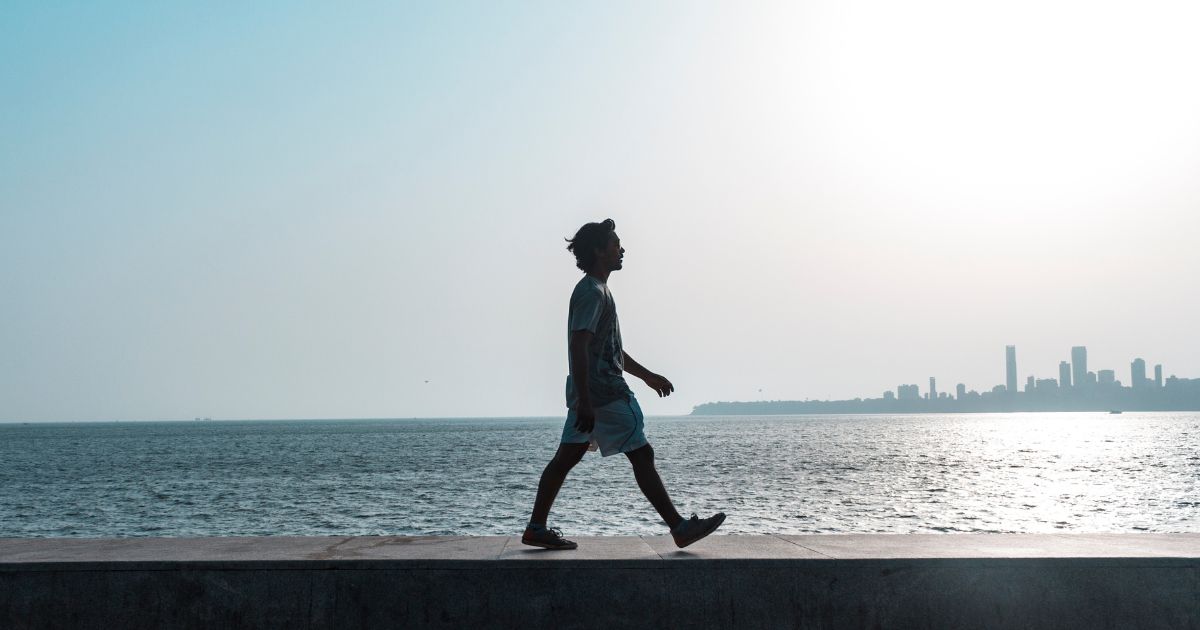 Person walking along a waterfront at sunrise, reflecting the body-mind journey toward clarity and healing.