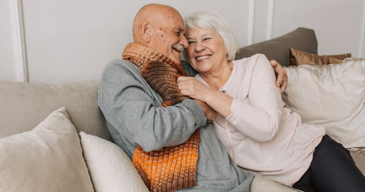 Older couple sharing a warm embrace on a couch, showing love, presence, and deep connection.