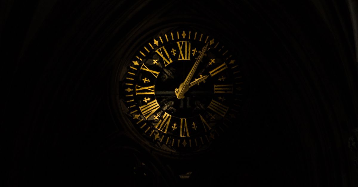 Antique clock face with gold Roman numerals showing the passage of time in a dark setting